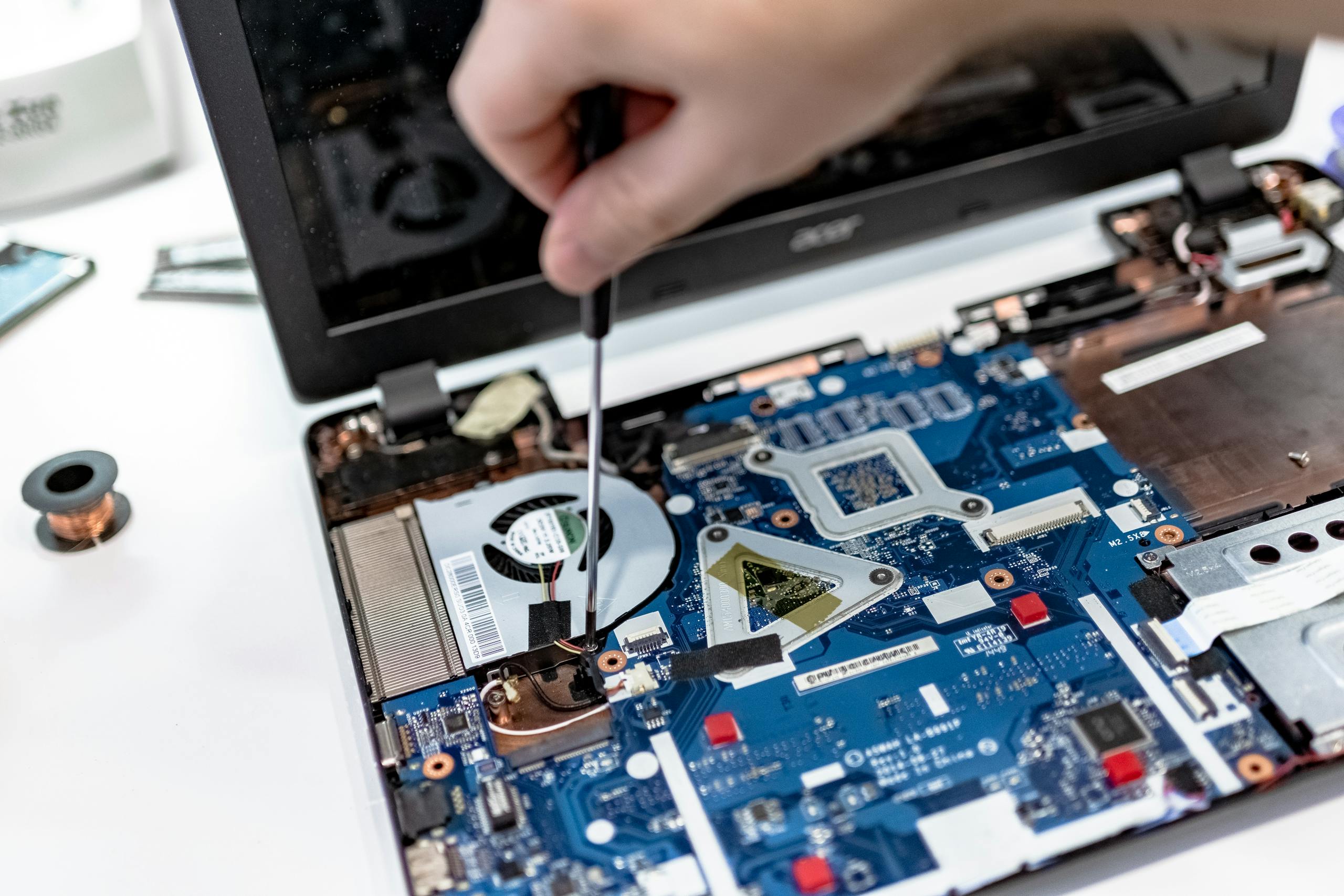 Hand repairing a laptop motherboard with a screwdriver, highlighting tech maintenance.