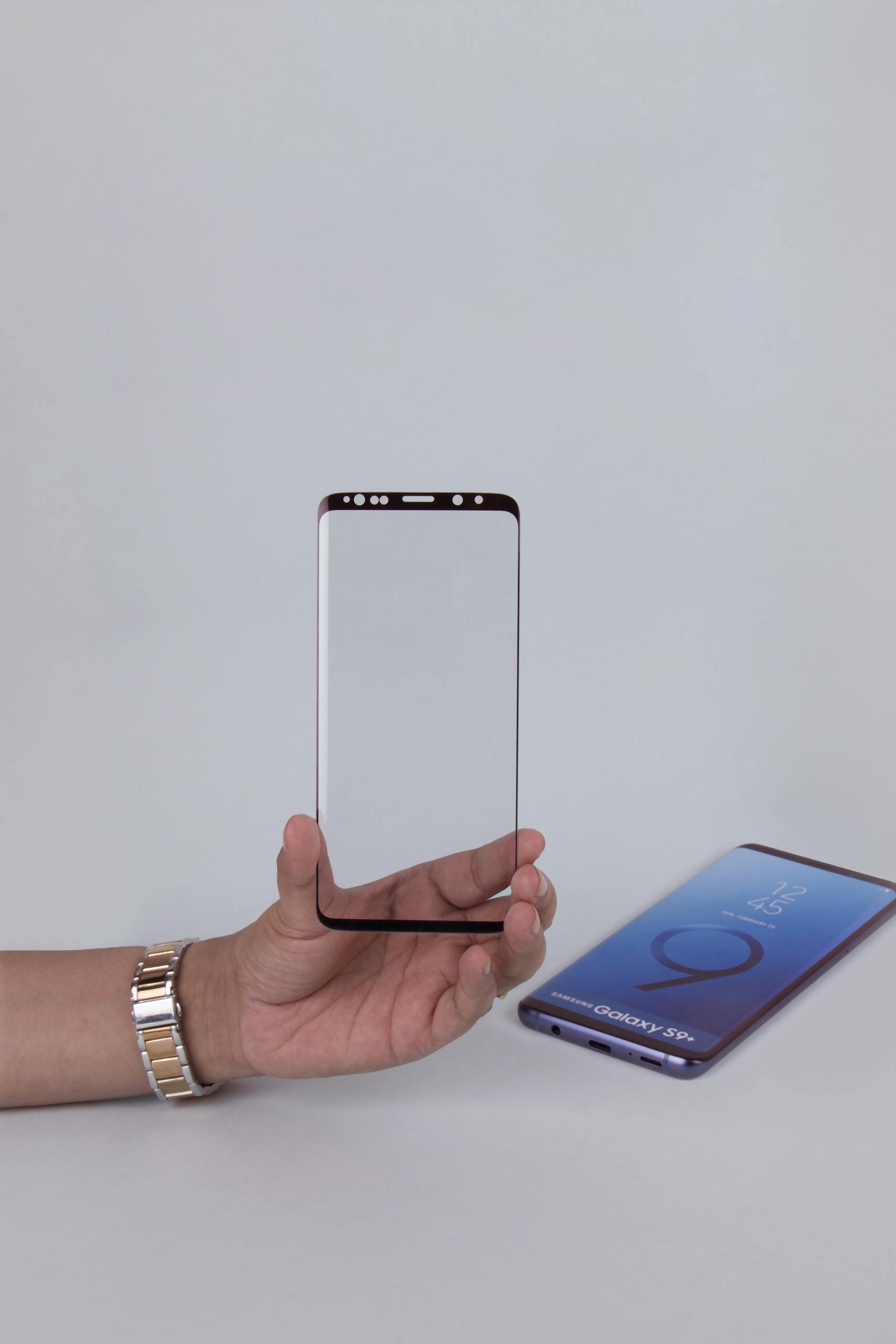 Close-up of a hand holding a tempered glass screen protector beside a smartphone.